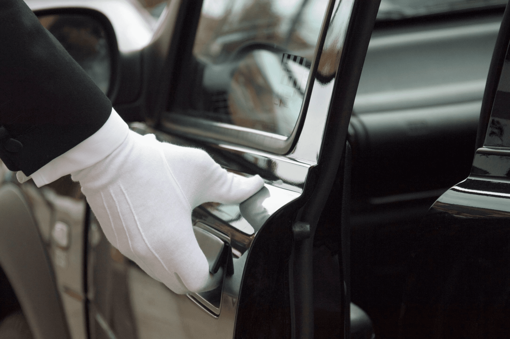 A person in white gloves opening the door of a car.