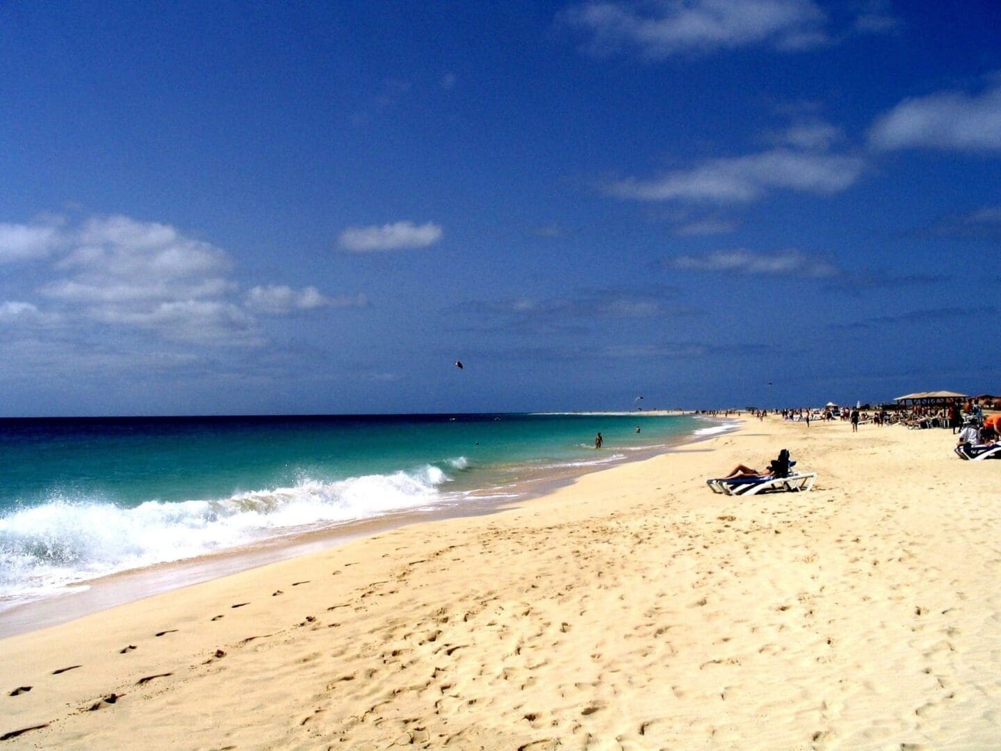 A beach with people sitting on the sand and waves coming in.